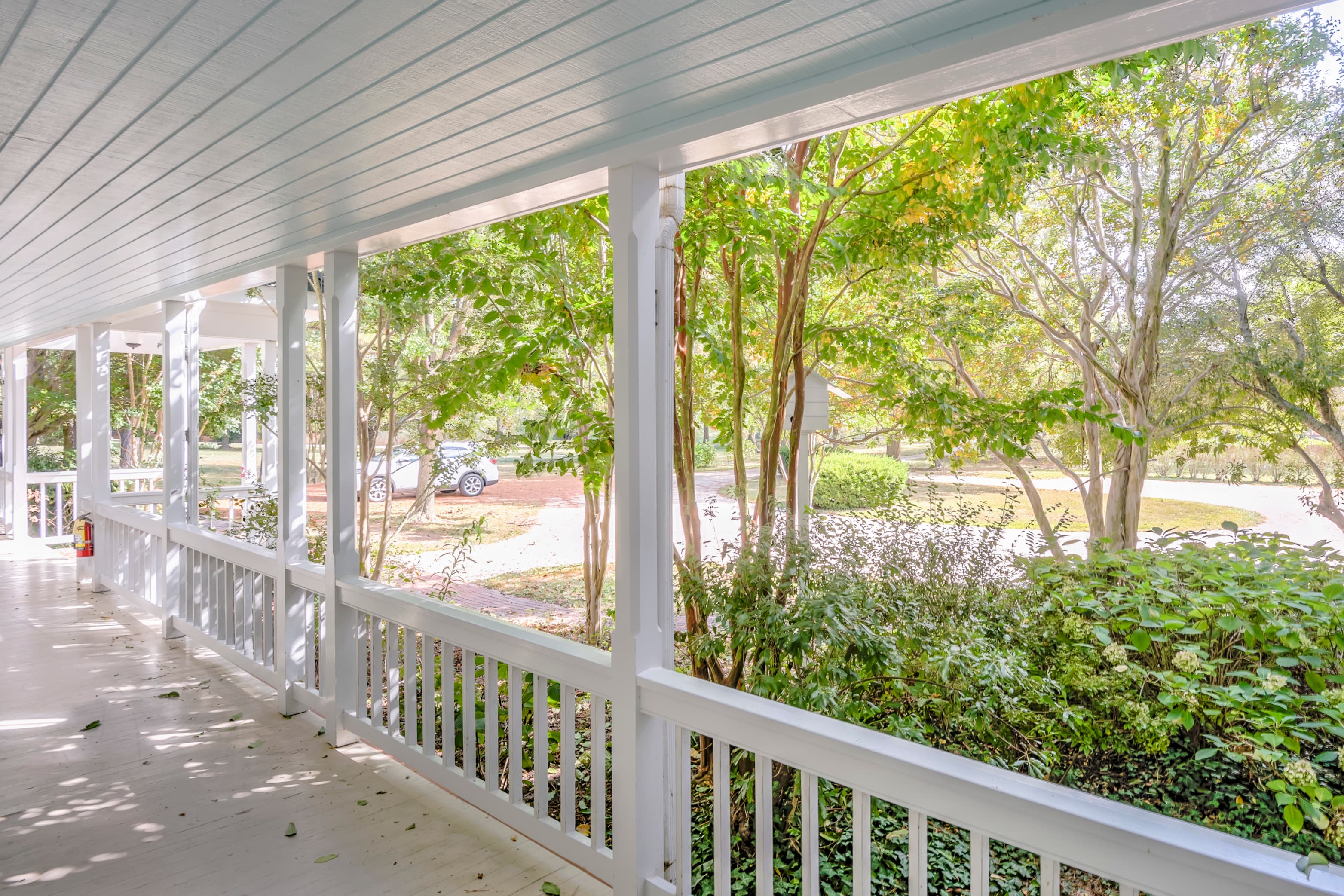 A porch with white railing overlooks a lush, green landscape and a quiet street.
