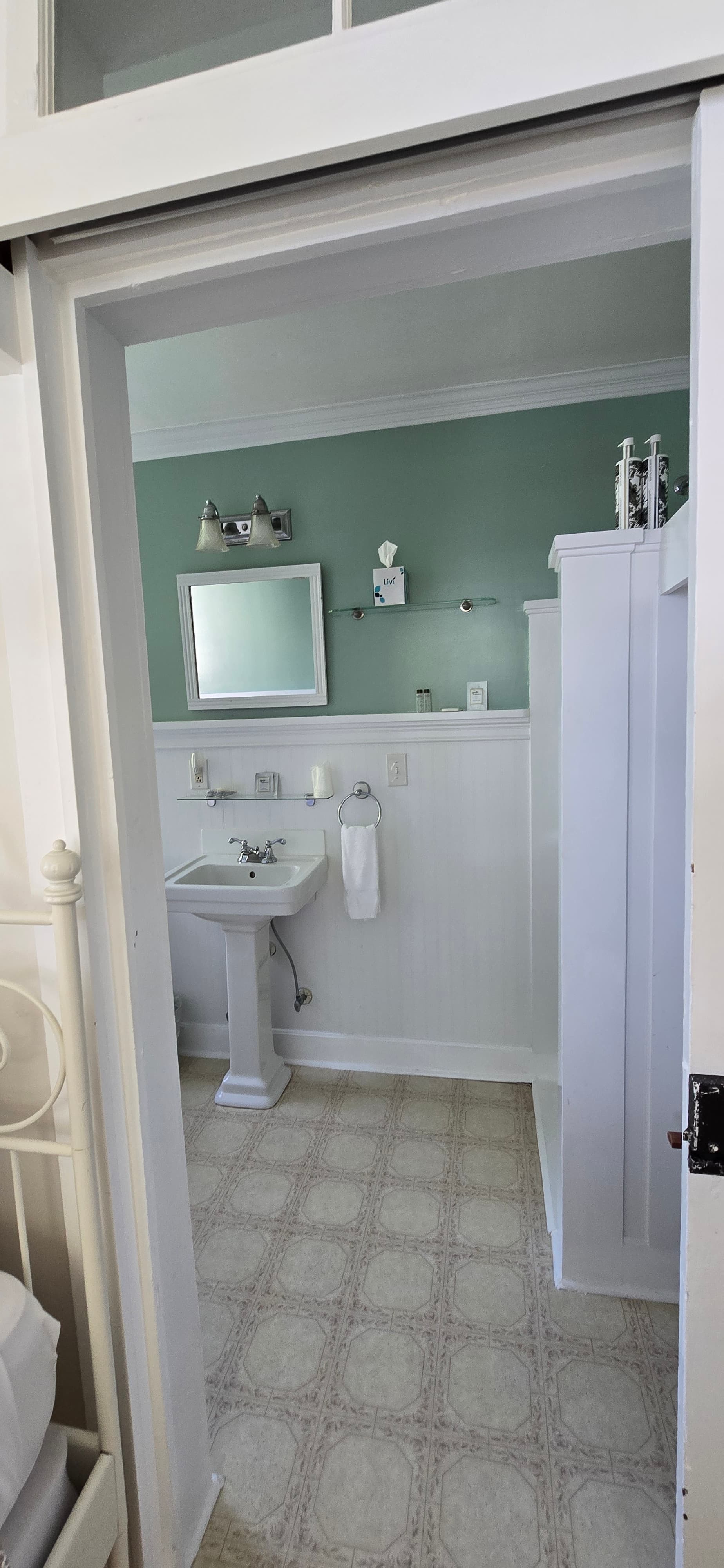 A view into a tidy bathroom featuring a sink, mirror, and light green walls.