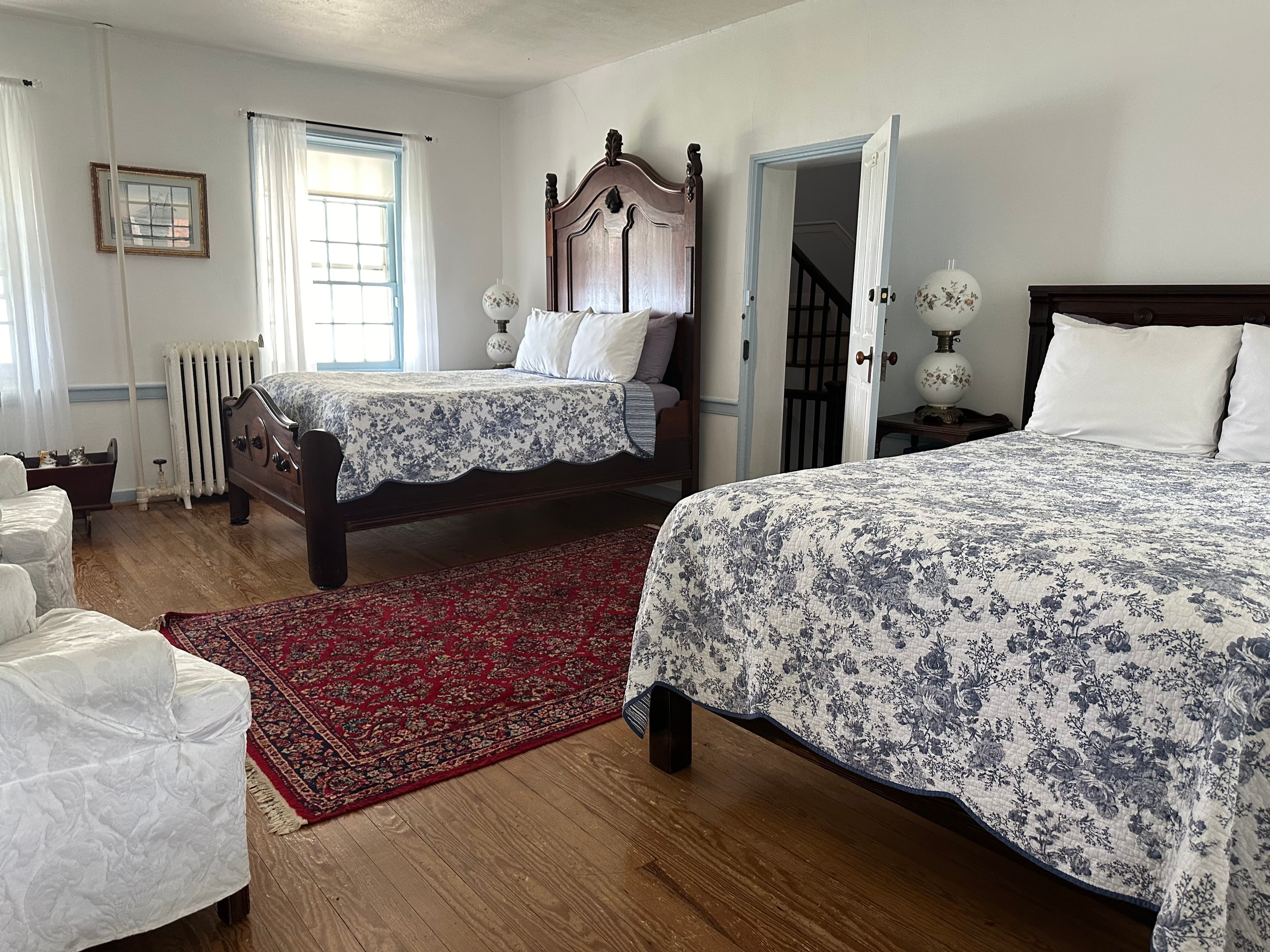 A spacious guest room featuring two beds with floral-patterned bedspreads, a red area rug, and ample natural light.