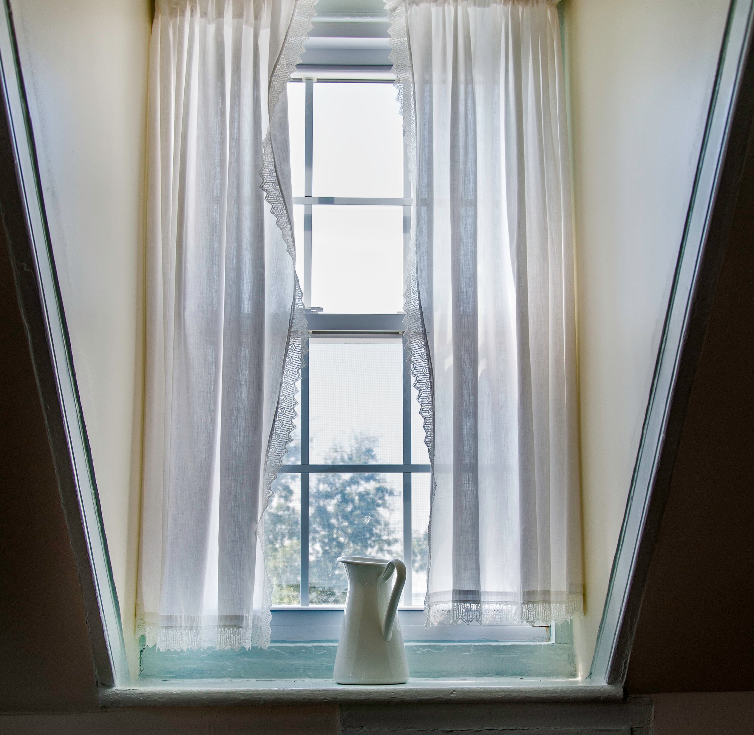 A minimalist window with sheer white curtains and a white pitcher on a ledge.