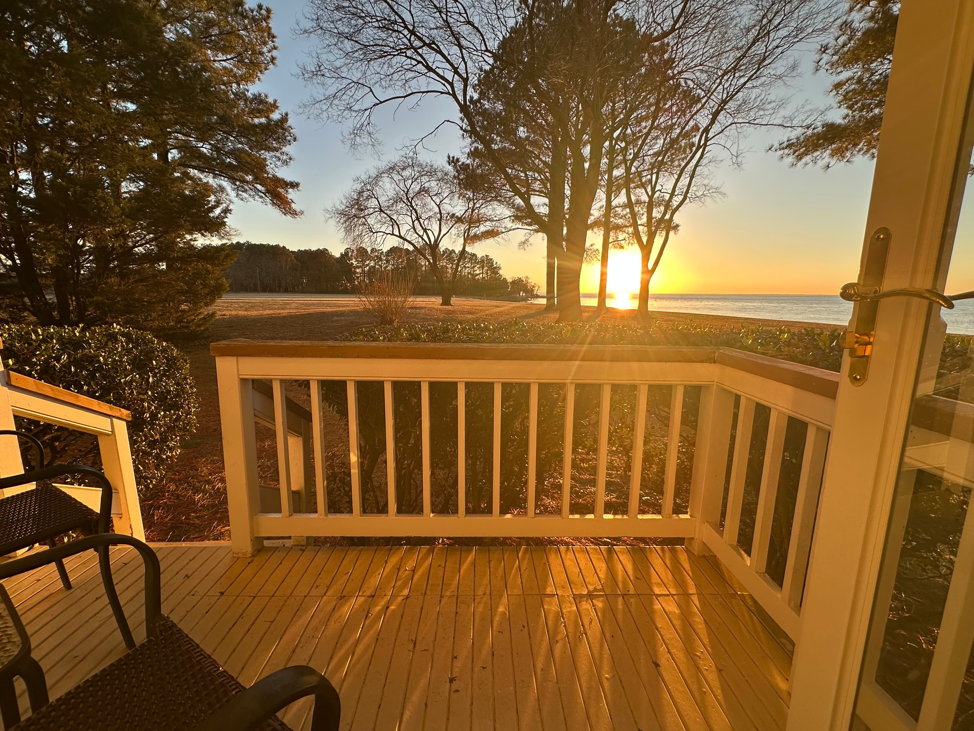 View of a sunrise over a beach from a wooden deck surrounded by trees.