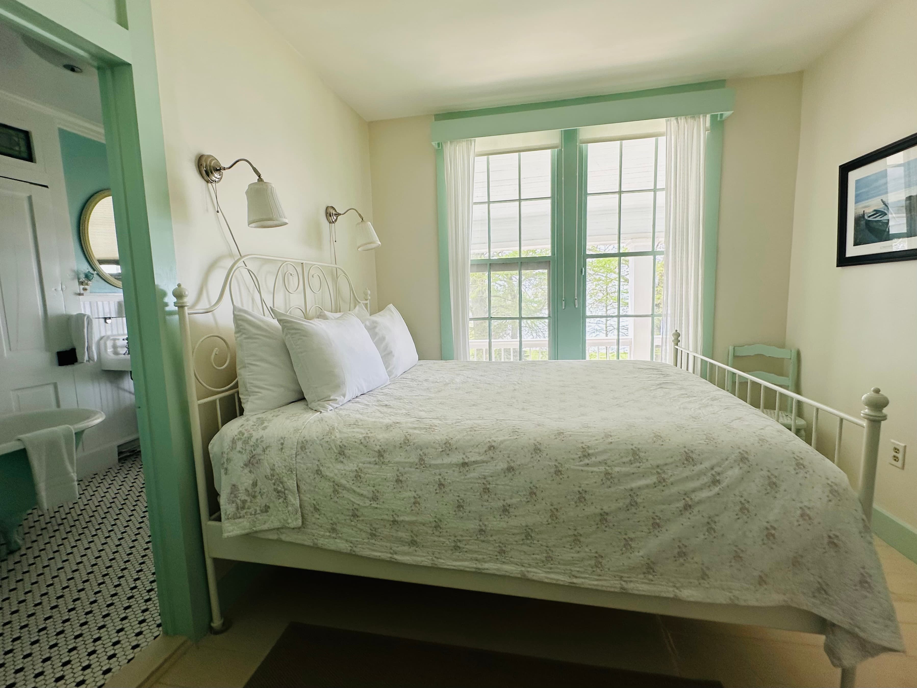A neatly arranged white bedroom featuring a metal bed frame, bright windows, and a light color scheme.