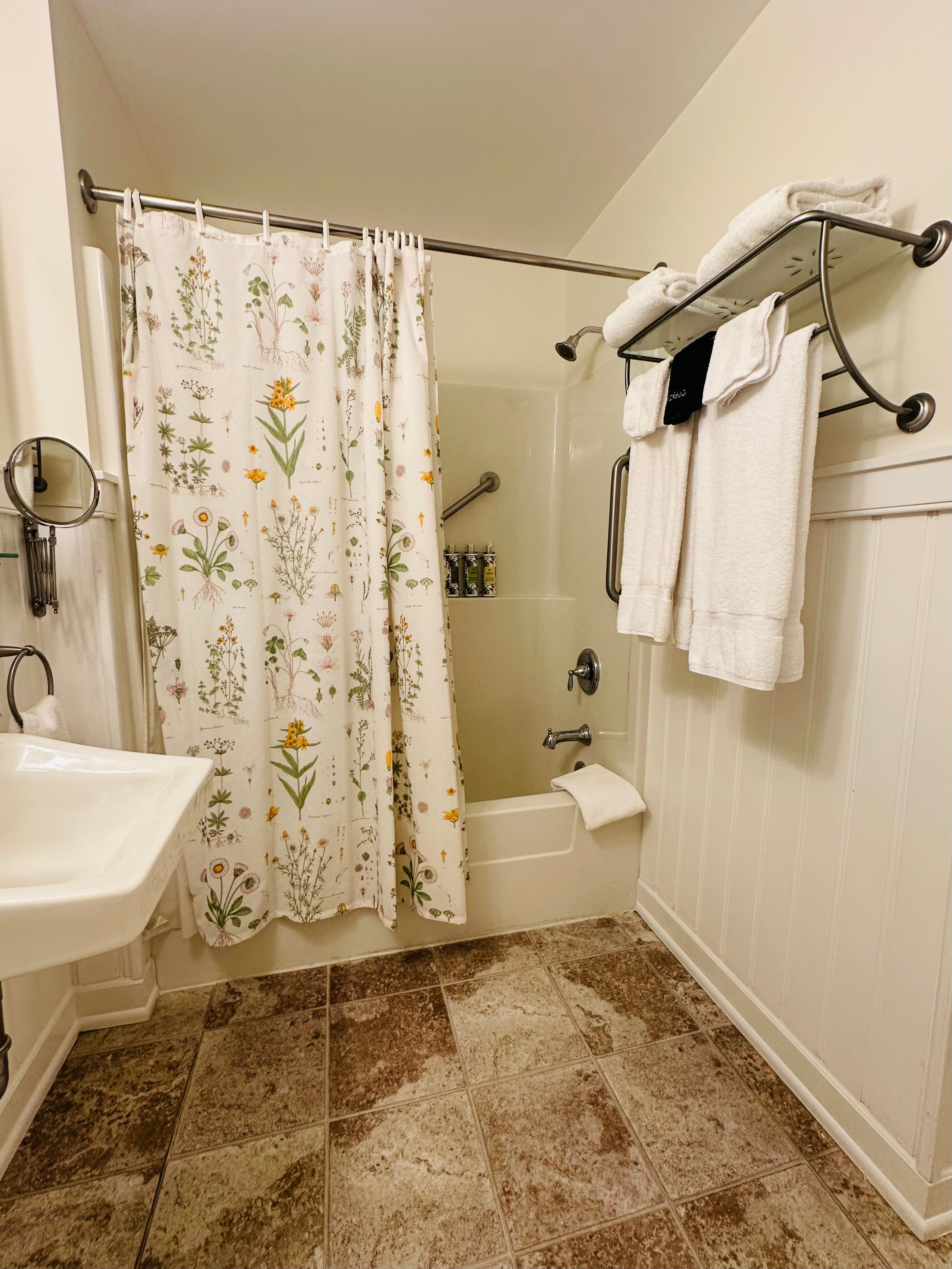 A bathroom featuring a floral shower curtain, towels on a rack, and a small sink.