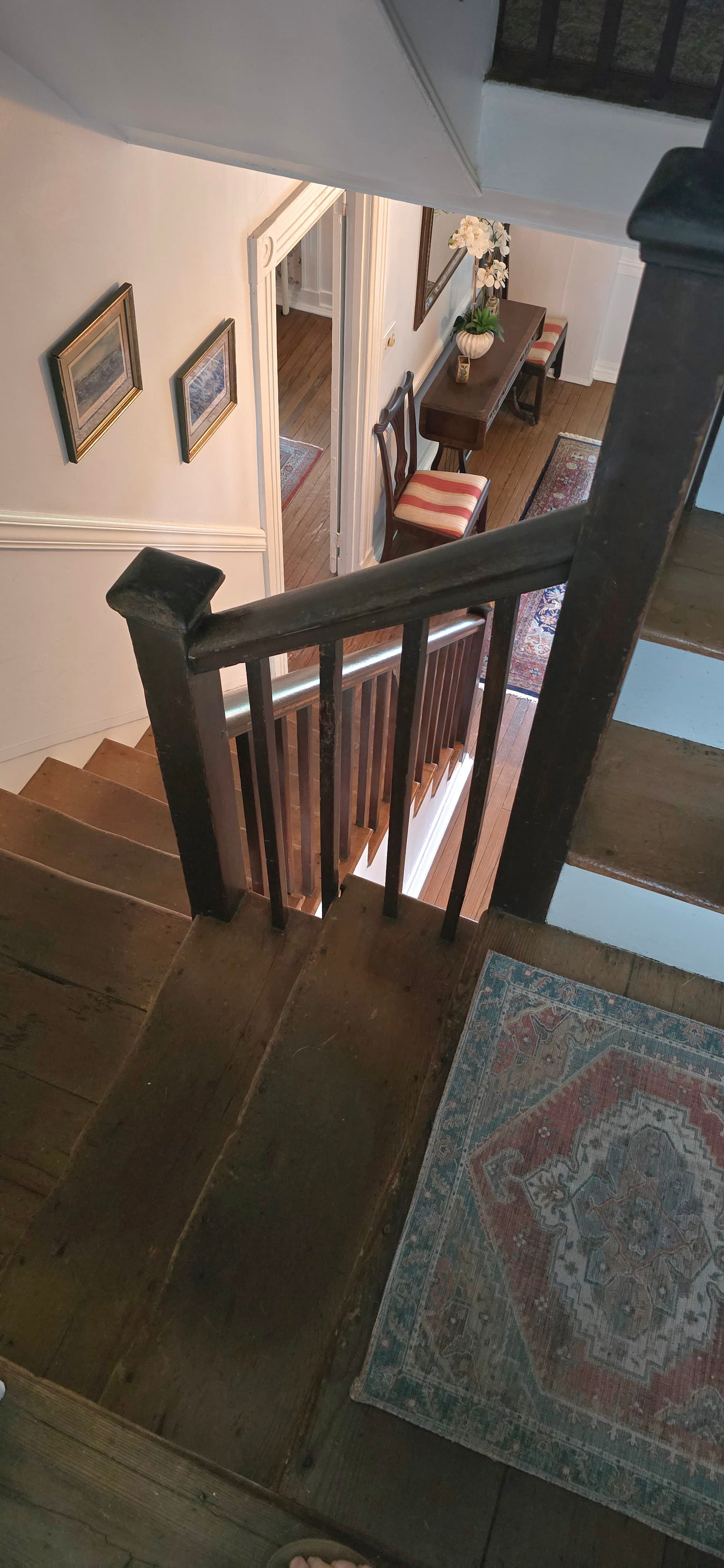A view of a staircase leading down to a hallway with framed pictures and a table.