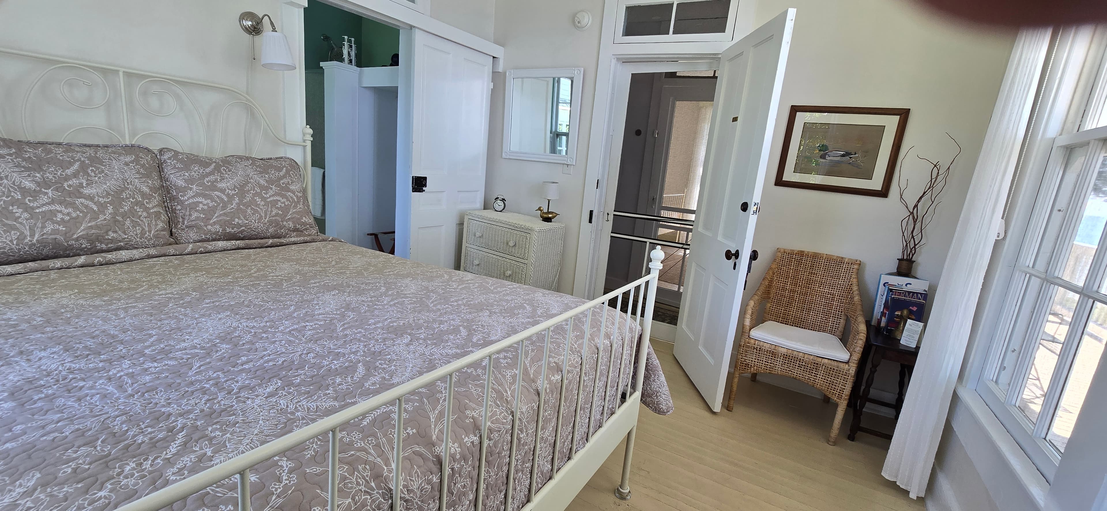 A cozy bedroom featuring a white metal bed, a wicker chair, and doors leading to an adjoining room.