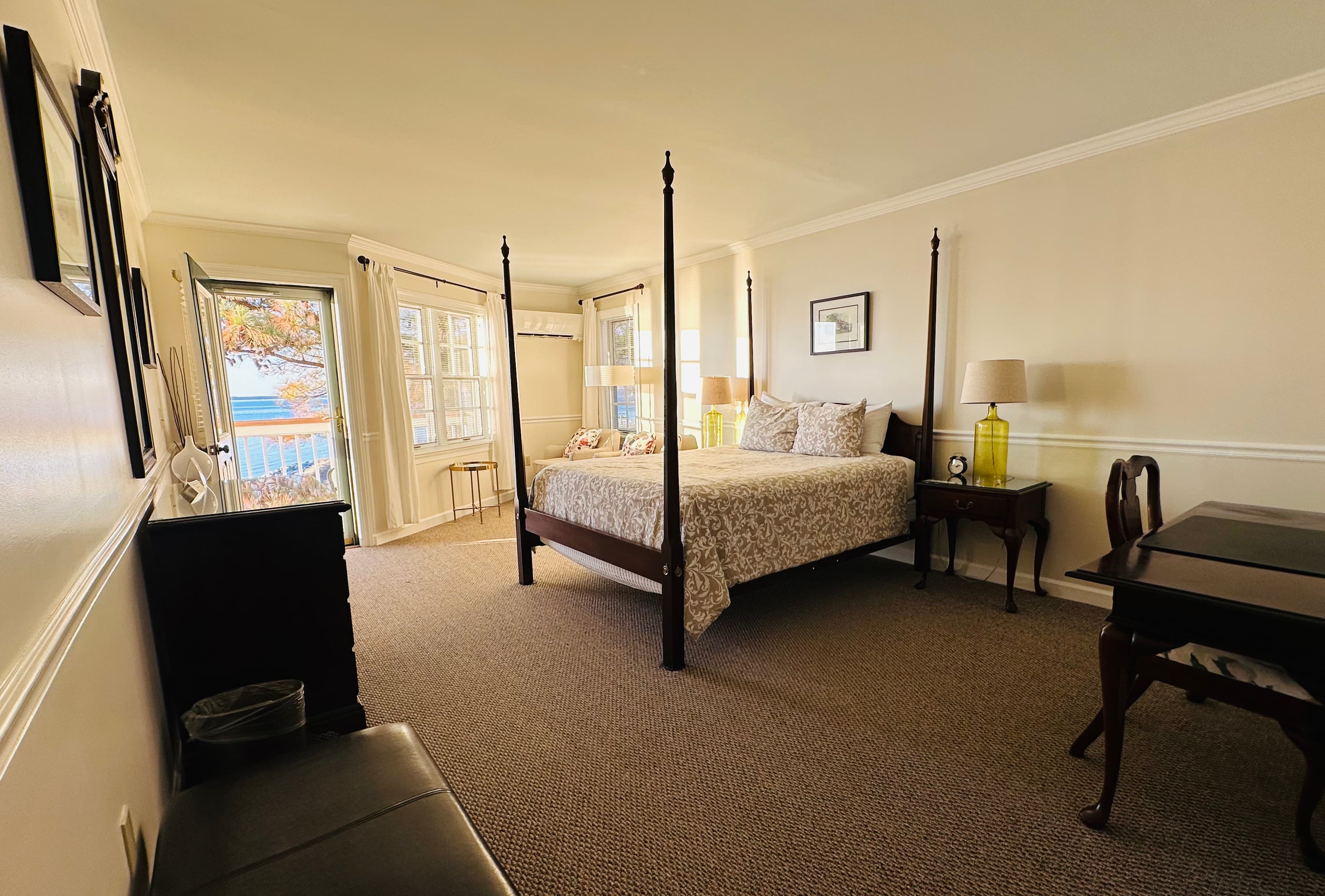 A spacious, well-lit bedroom featuring a four-poster bed, a desk, and large windows.