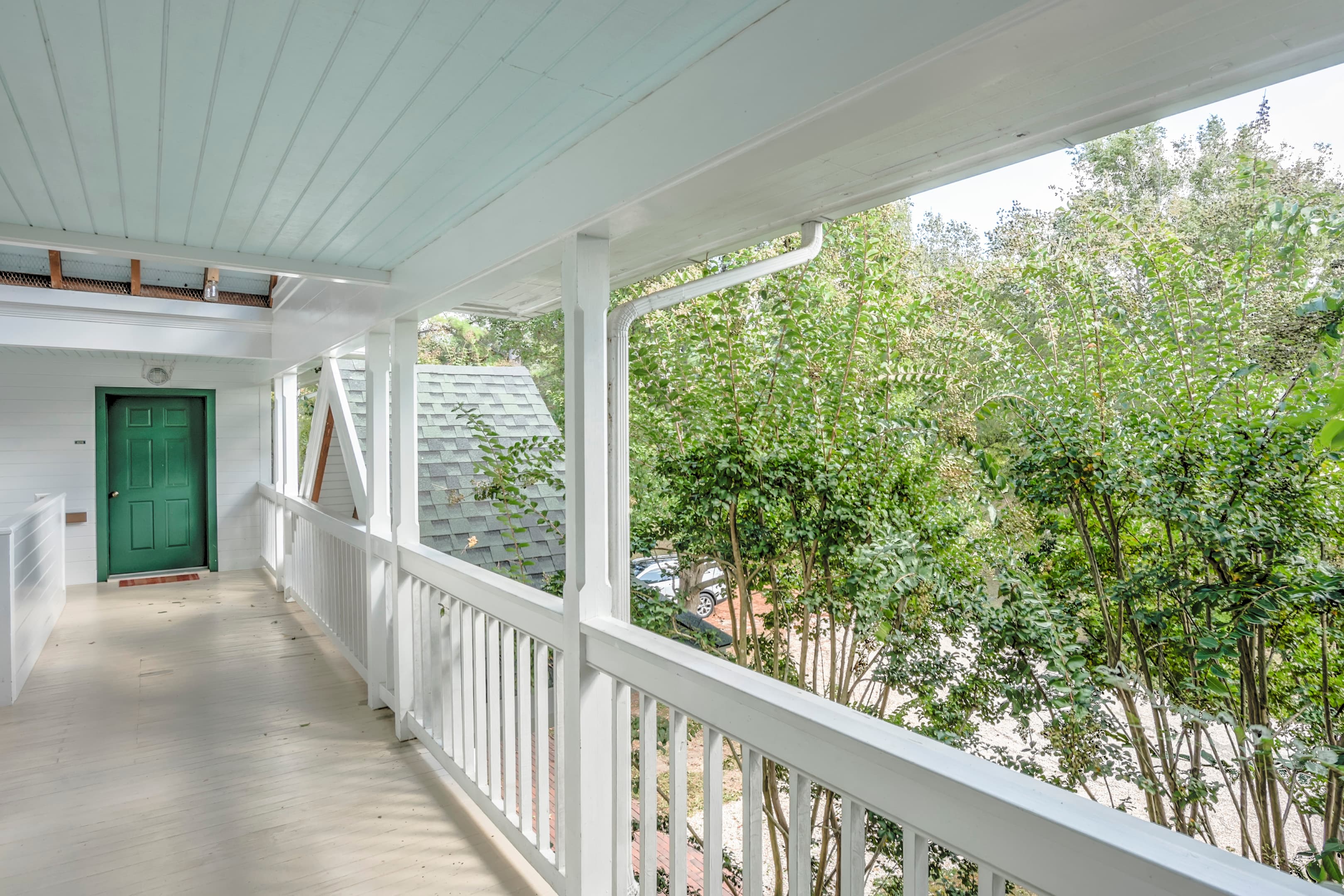 A bright, airy balcony with white railings and a green door, surrounded by lush greenery.