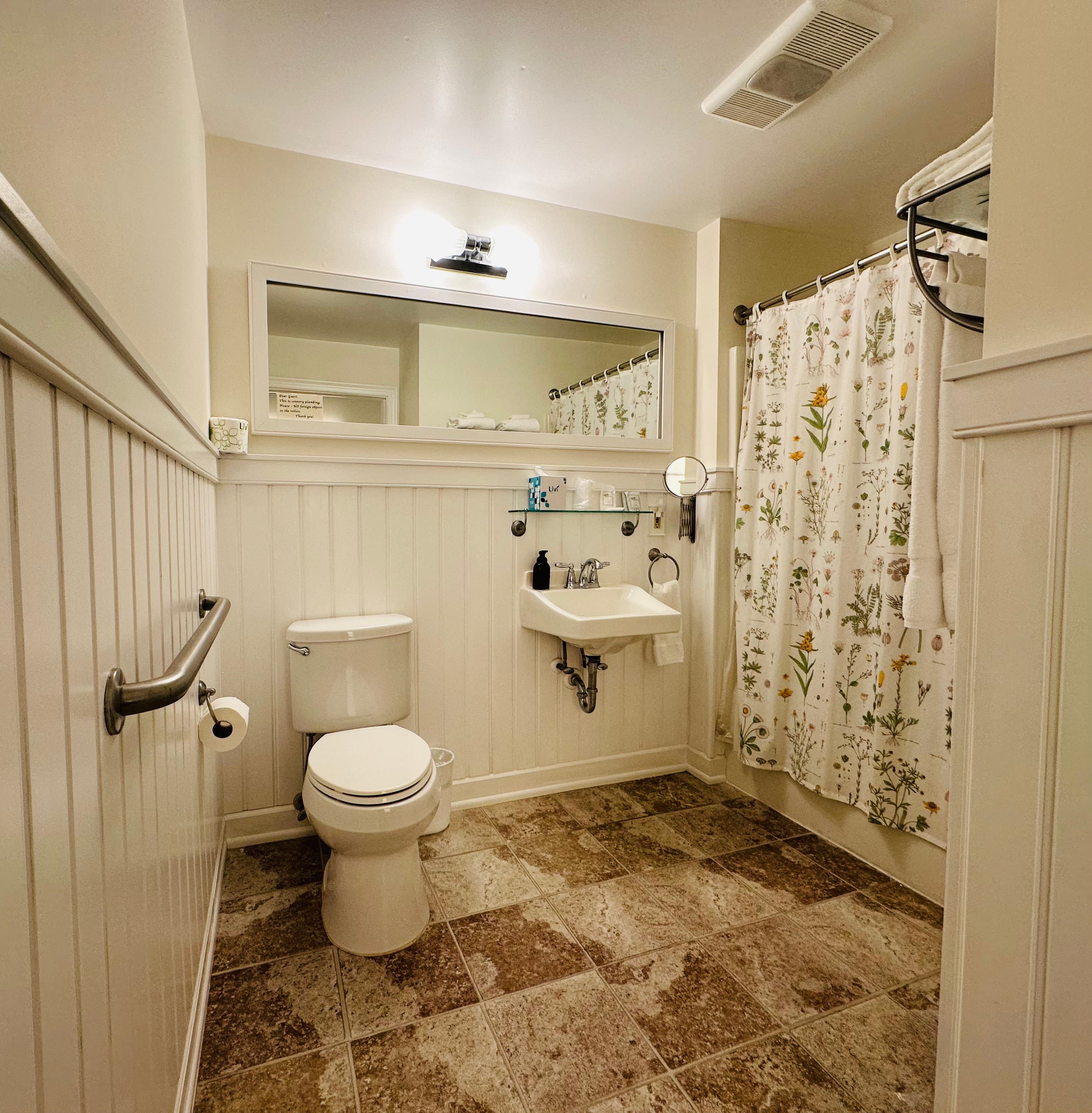 A compact bathroom featuring a toilet, sink, mirror, and floral shower curtain.