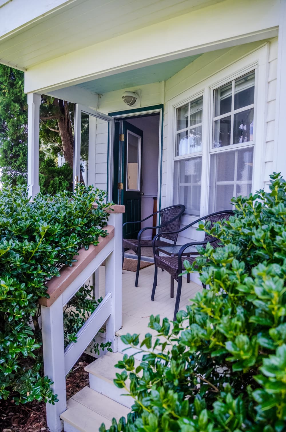 A serene porch with two chairs flanked by lush greenery and a welcoming doorway.