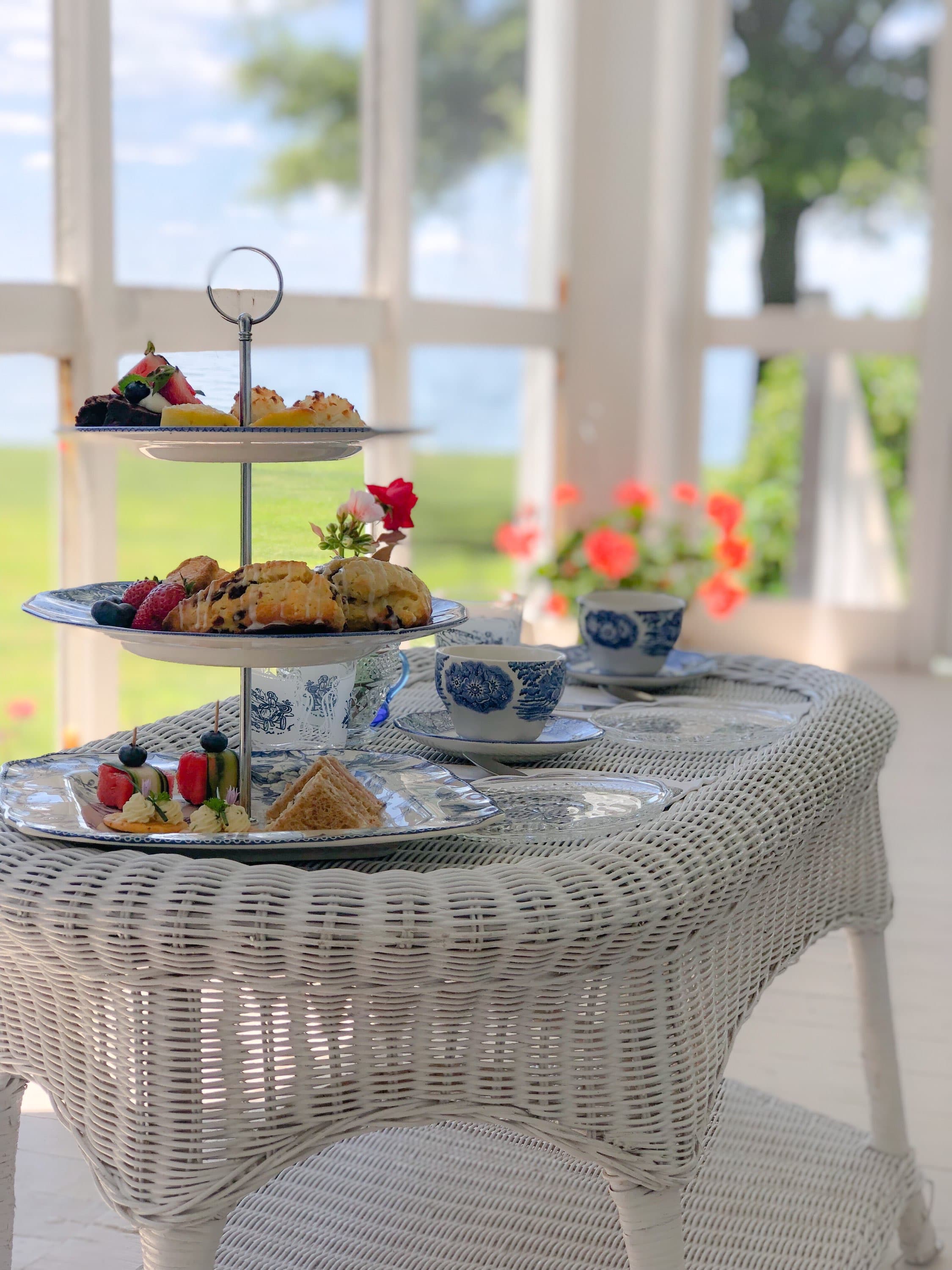 A charming afternoon tea set with pastries and tea cups on a white wicker table, surrounded by a scenic view.