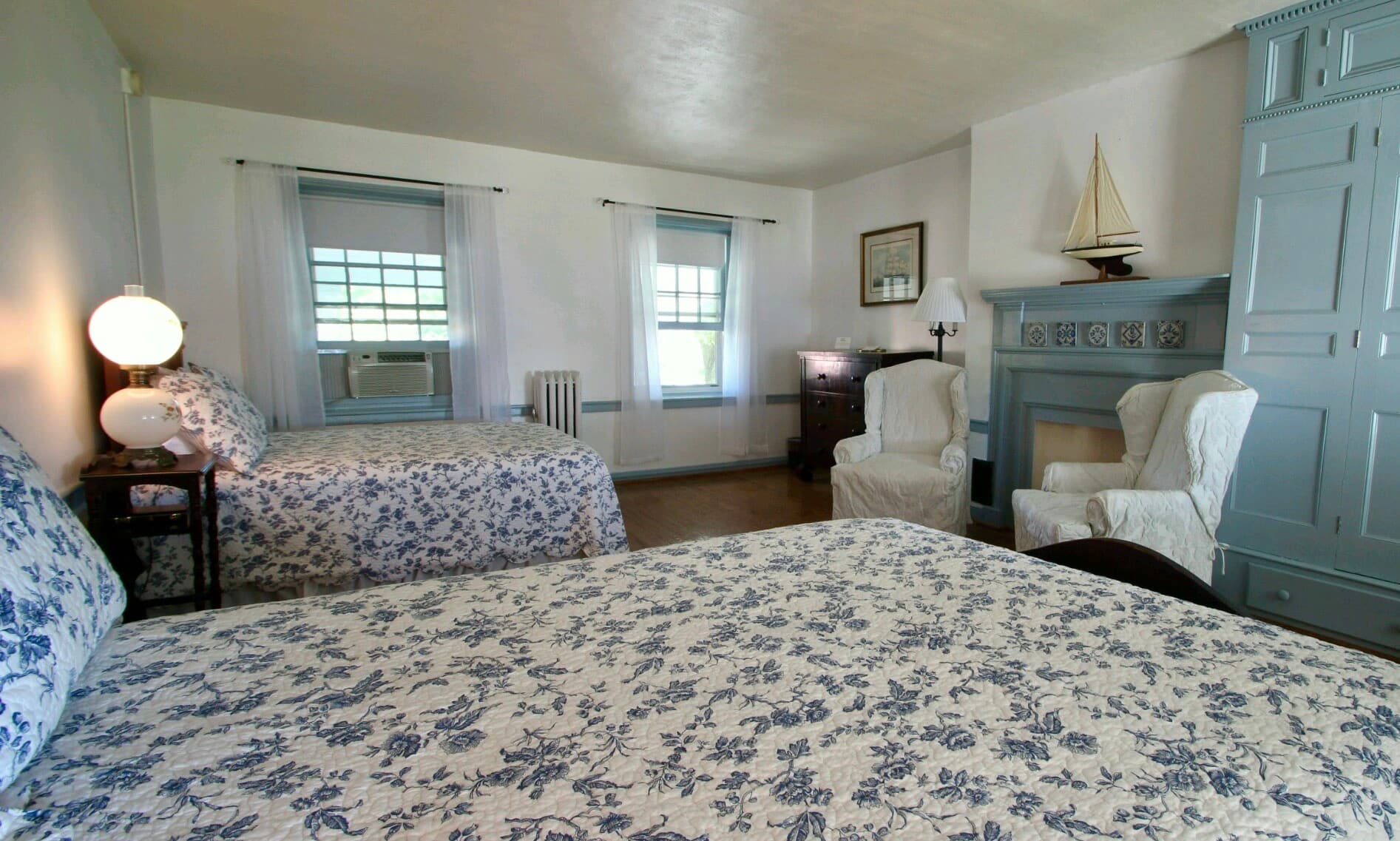 A cozy bedroom featuring two floral-patterned beds, a fireplace, and comfortable seating.