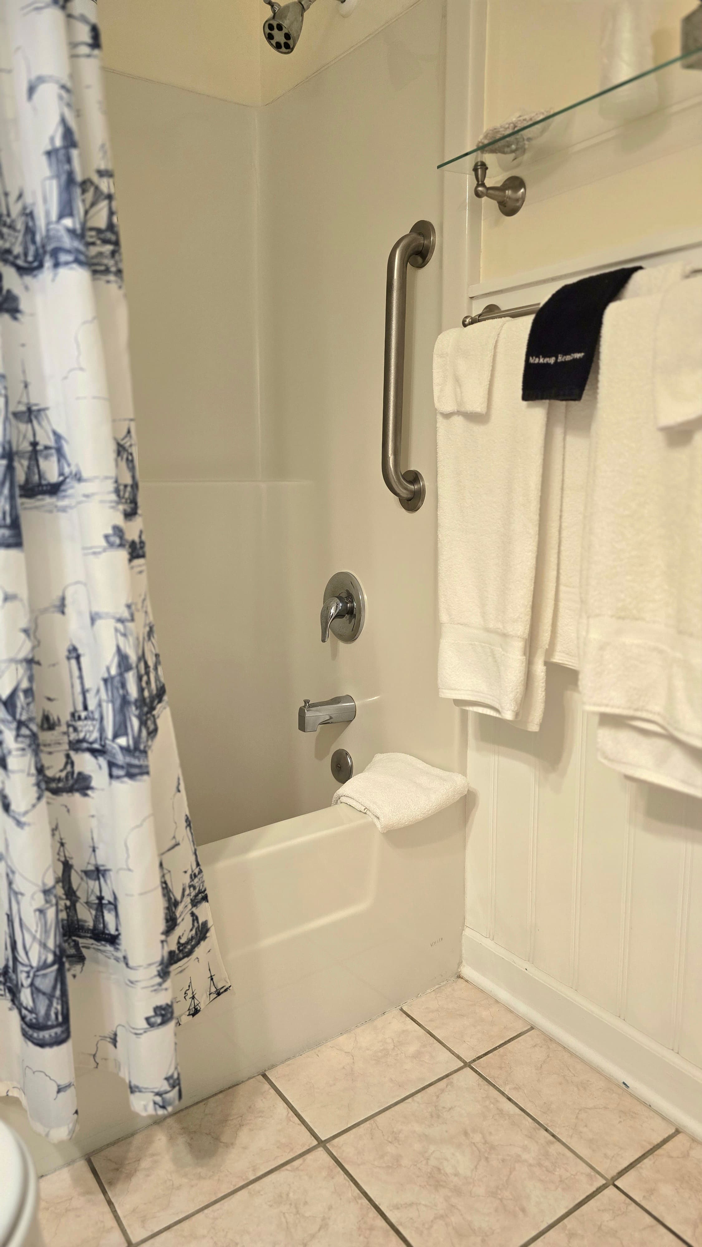 A bathroom with a shower area, nautical-themed curtain, and neatly arranged white towels.