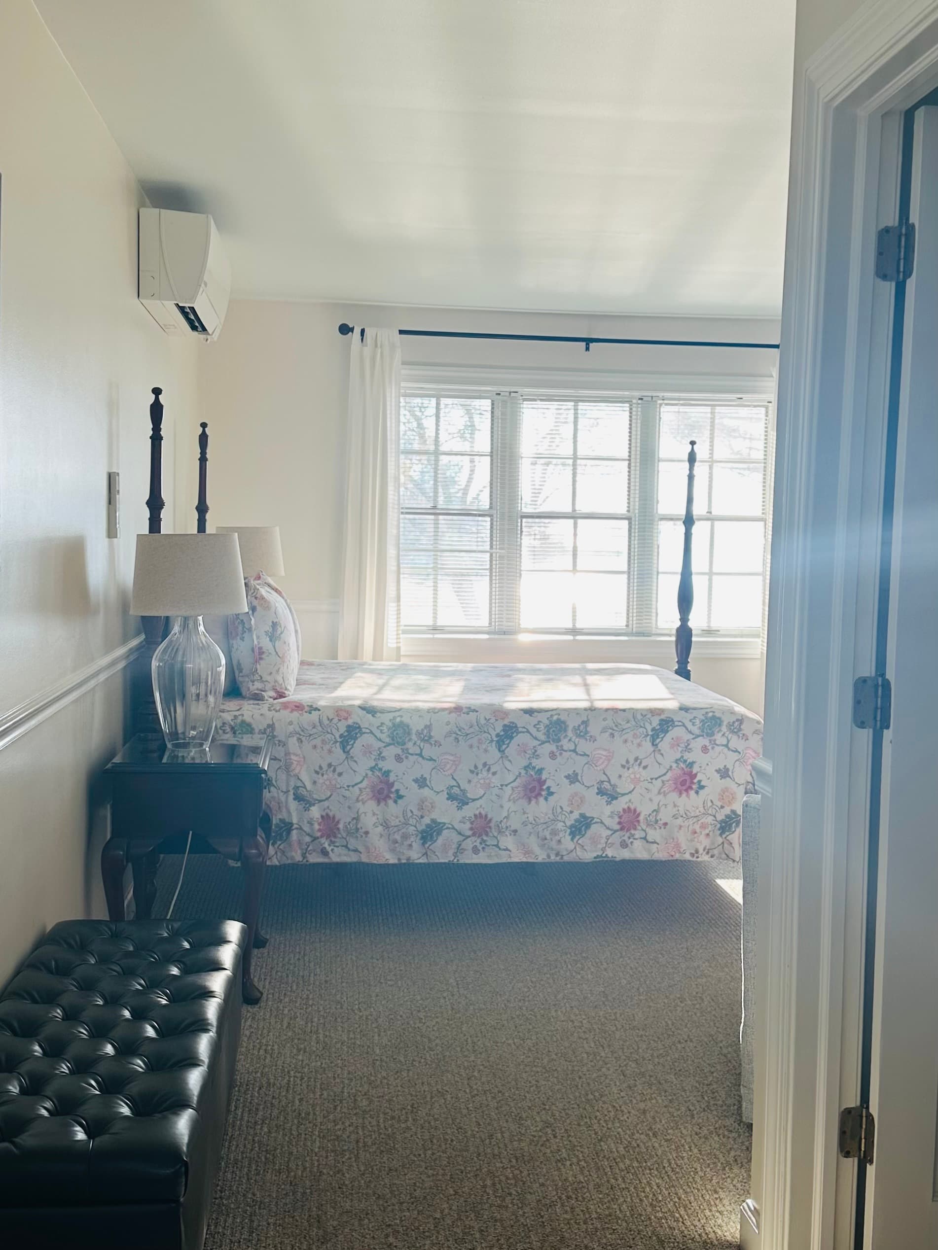 Bright bedroom with floral bedding, a wooden bed frame, and natural light streaming through large windows.