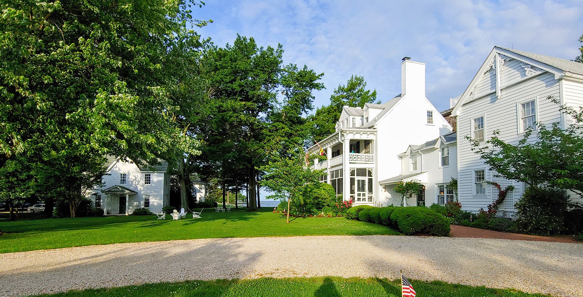A picturesque white house surrounded by lush greenery and a gravel driveway.