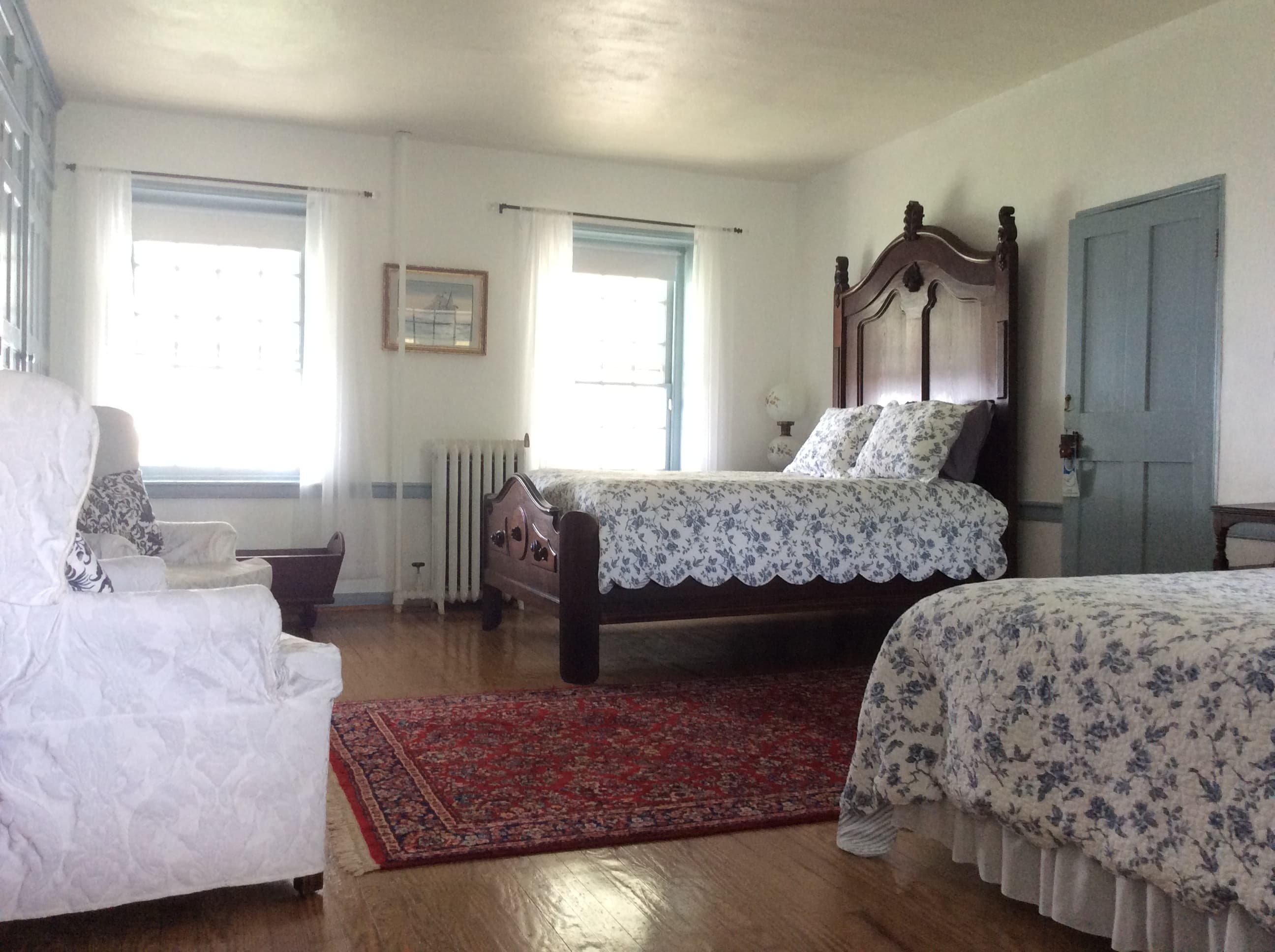A light-filled bedroom featuring two beds with floral bedding and a cozy sitting area.