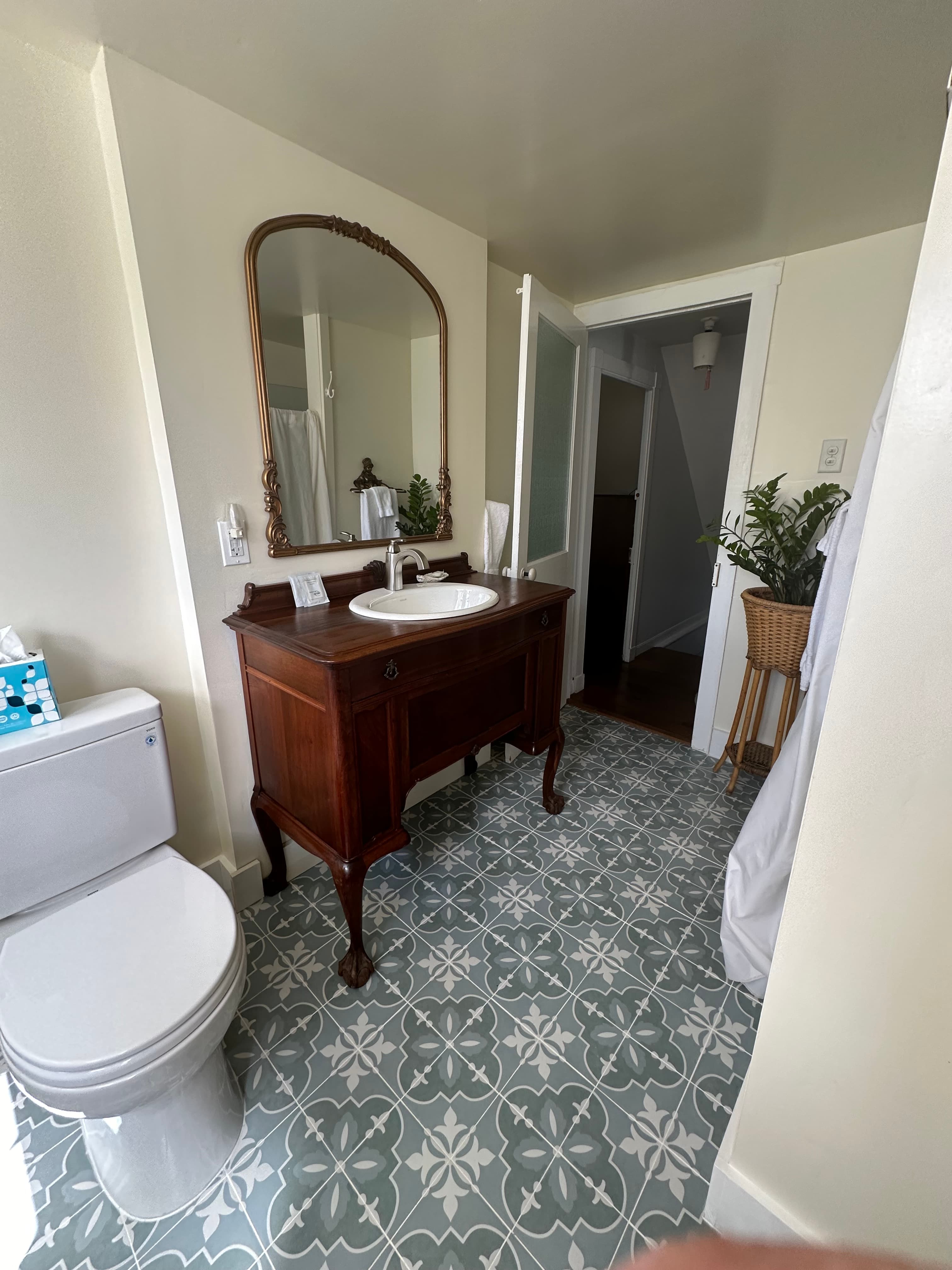 A bright bathroom featuring a wooden vanity with a sink, a toilet, and decorative tile flooring.
