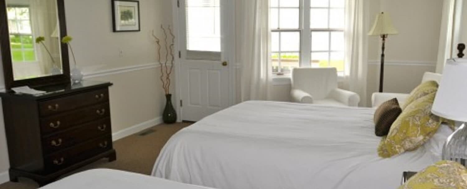 A bright, inviting bedroom featuring two beds, a dresser, and a cozy armchair by the window.