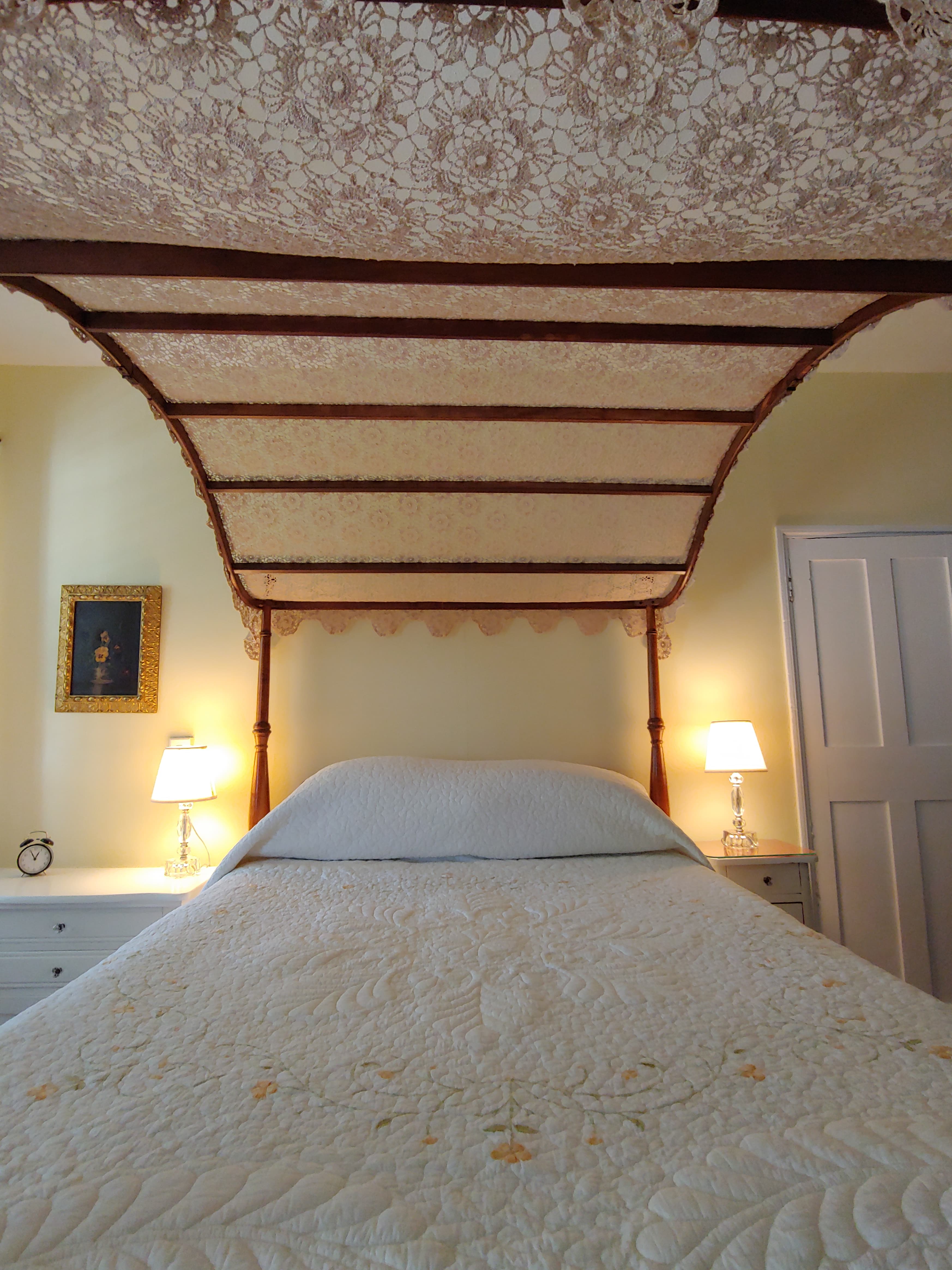 A cozy bedroom featuring a canopied bed, bedside lamps, and a framed artwork on the wall.