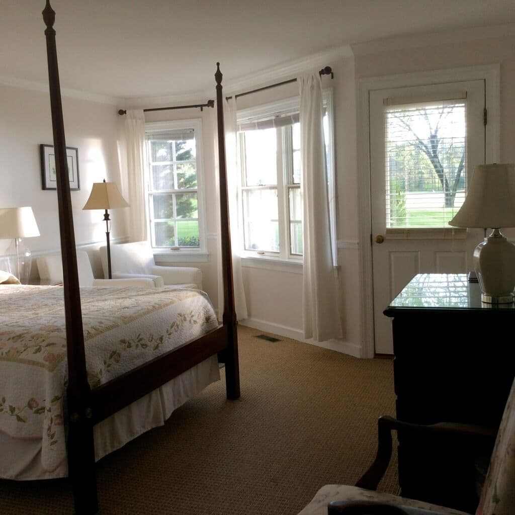Bright and airy bedroom featuring a four-poster bed, large windows, and tasteful furnishings.