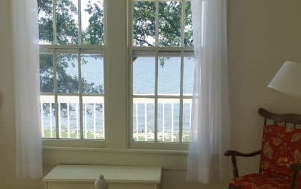 A bright room with two large windows revealing a view of water and greenery outside.