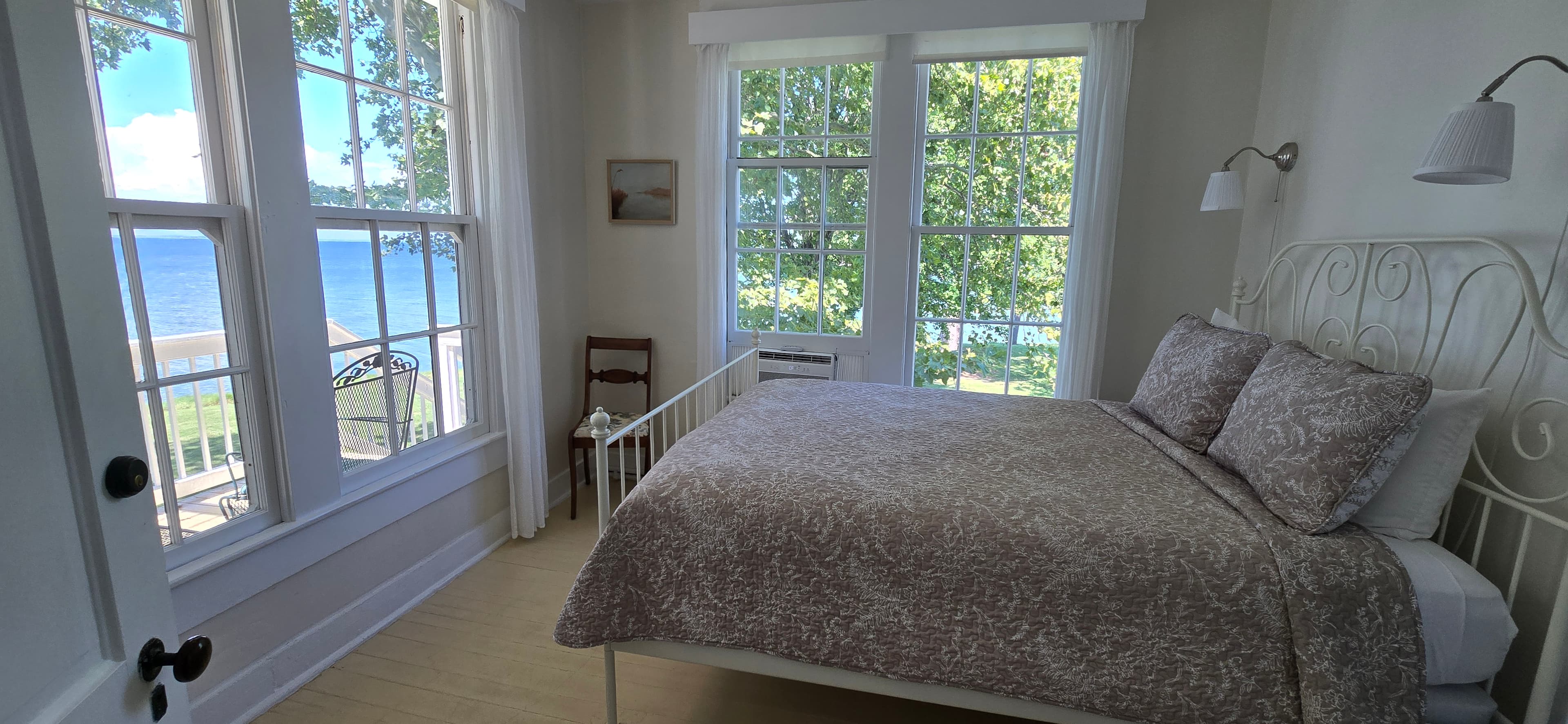 Bright bedroom with a white bed, large windows, and a view of a lake.