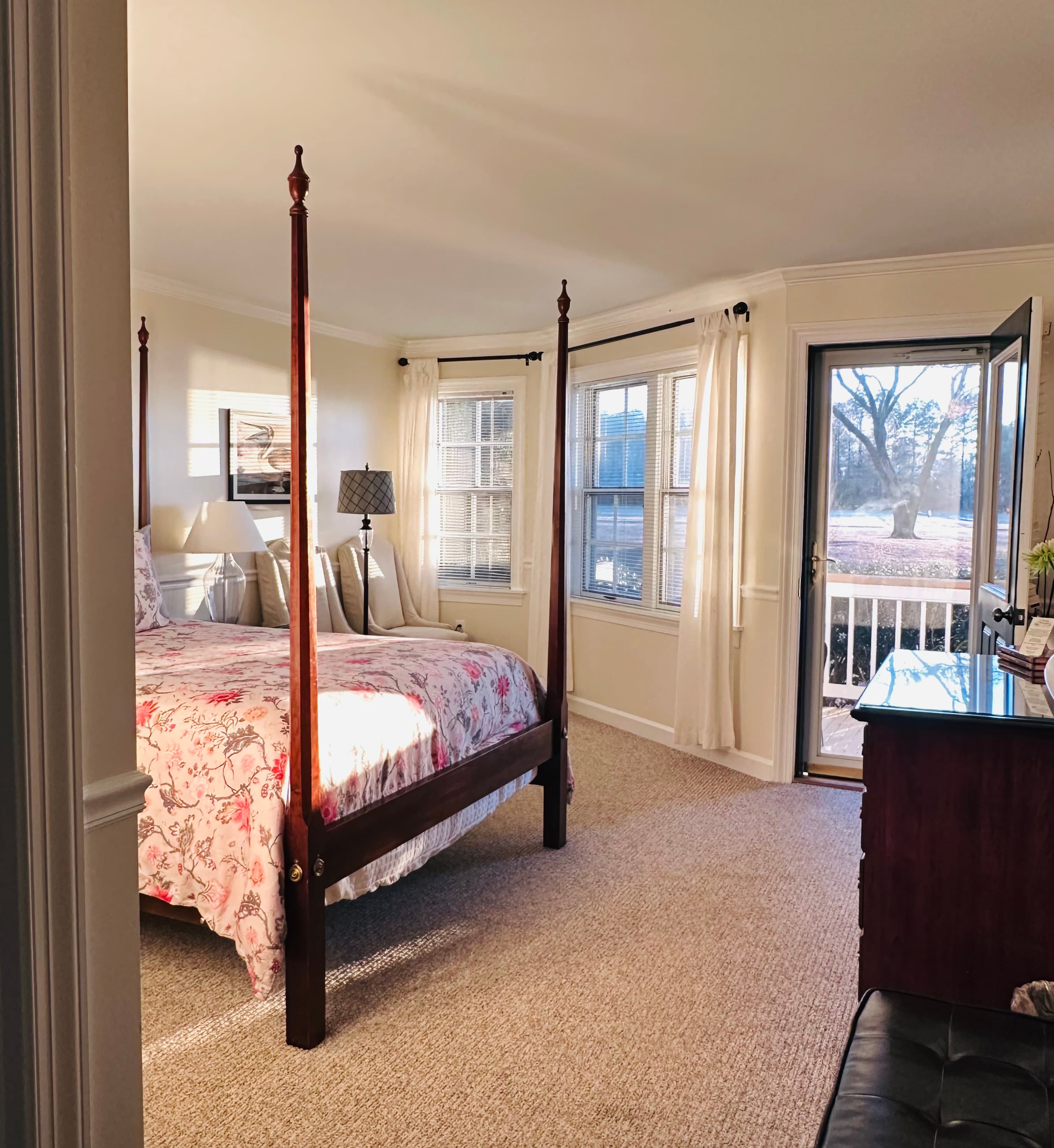 Bright bedroom featuring a four-poster bed, large windows, and an open door leading to a balcony.