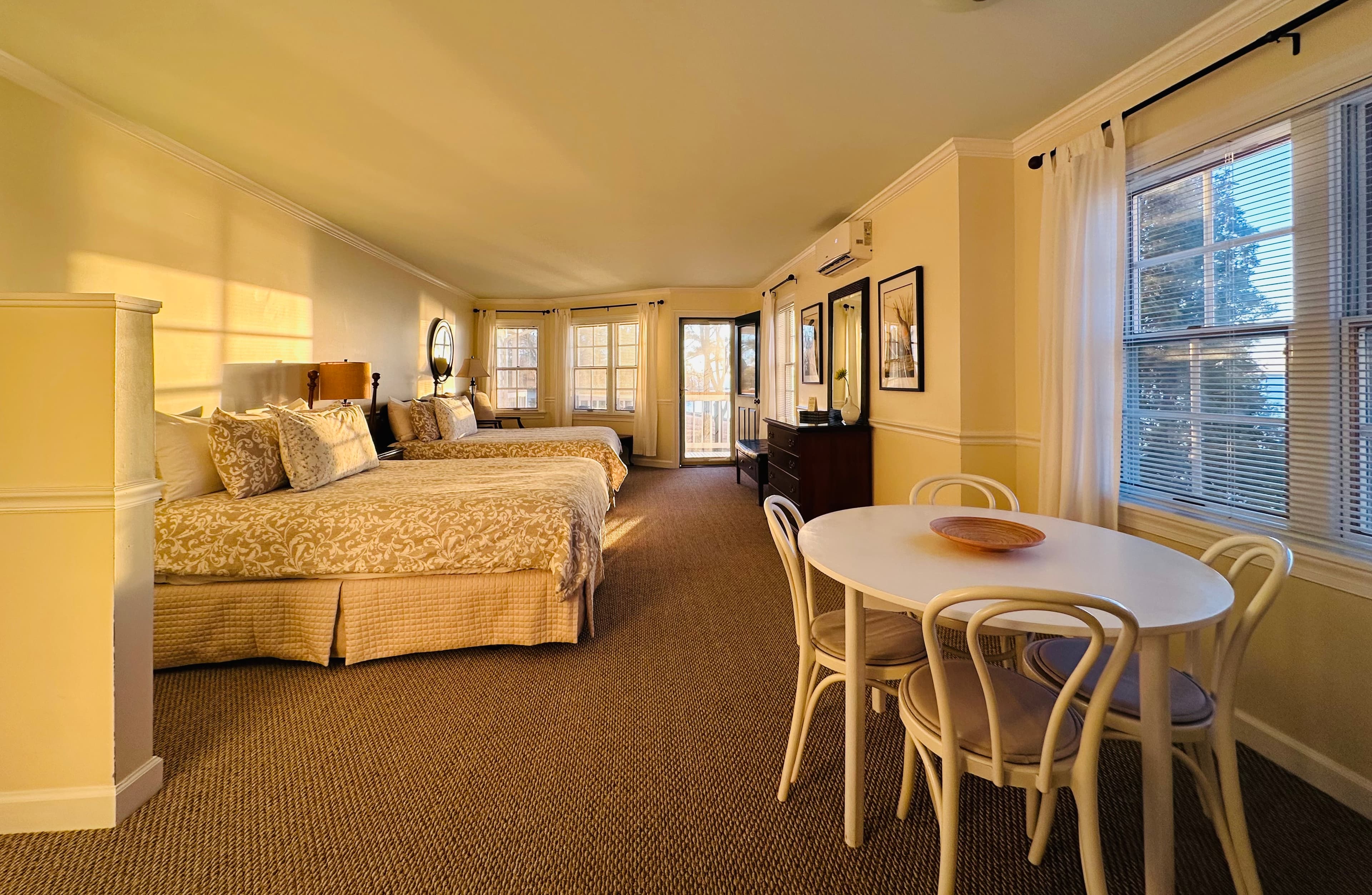 A spacious hotel room featuring two queen beds, a dining table, and large windows allowing natural light.