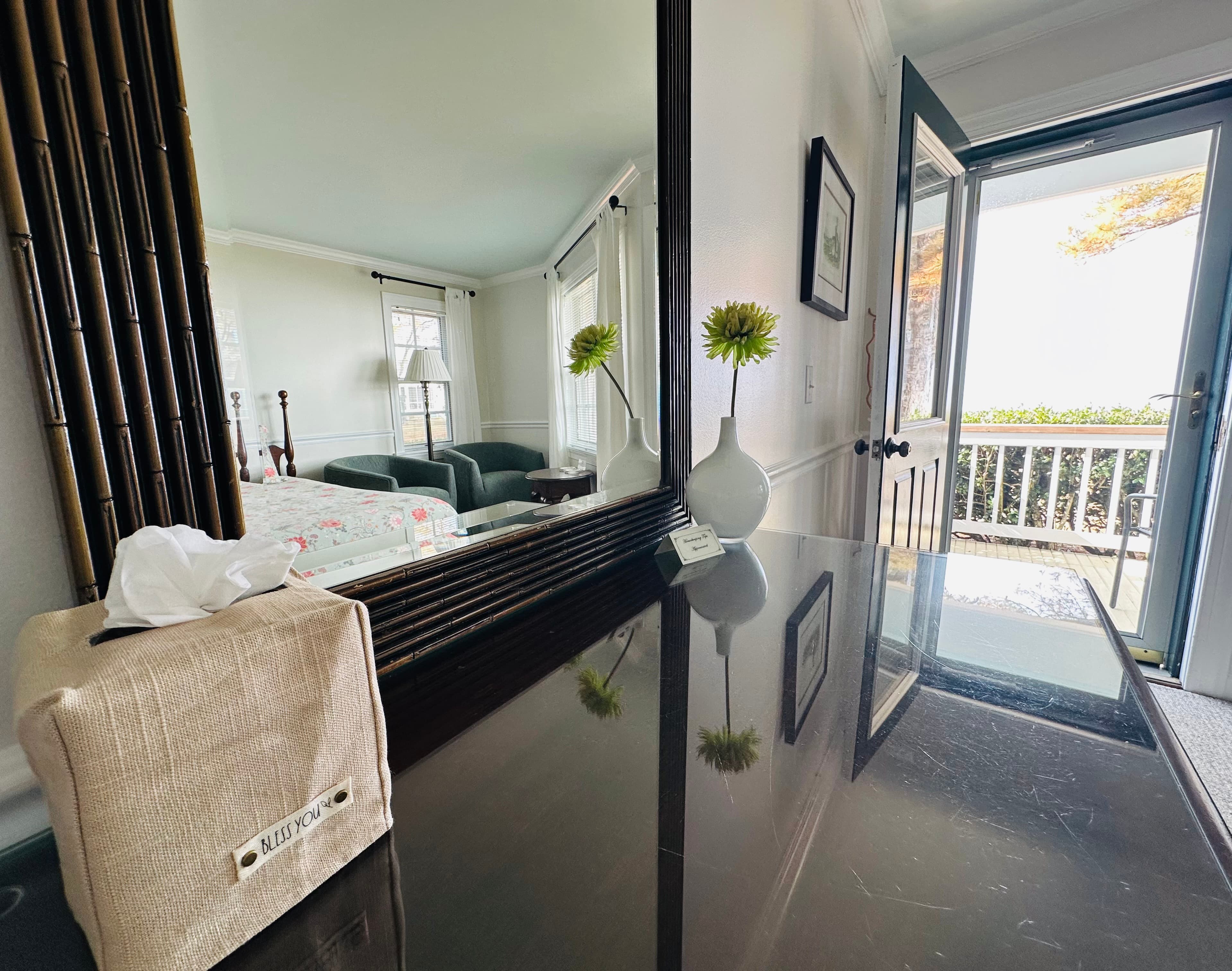 A mirror reflects a room with a couch and a doorway leading outside, alongside a vase and tissue box on a table.