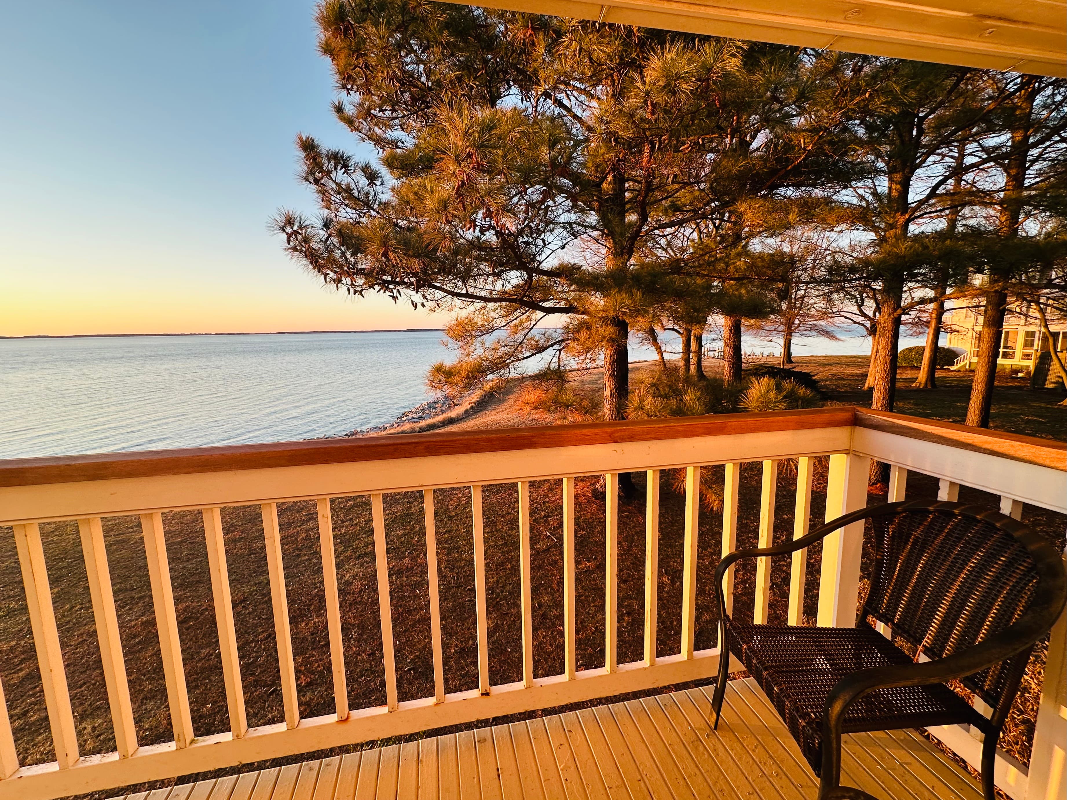 A peaceful view of a lakeside scene from a wooden balcony with a black chair.