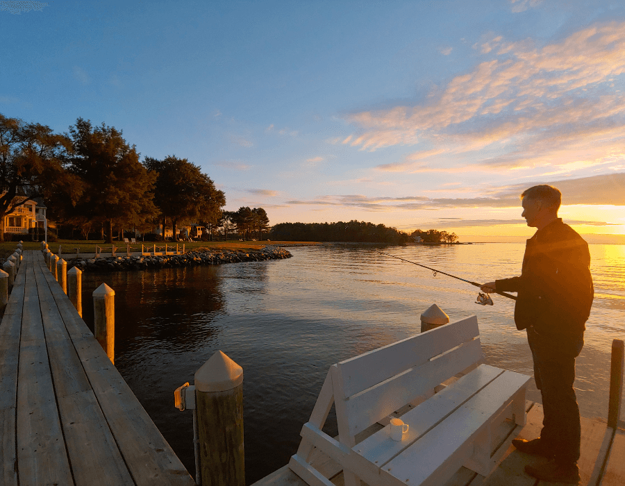 A man stands on a dock at sunset, fishing peacefully by the water.