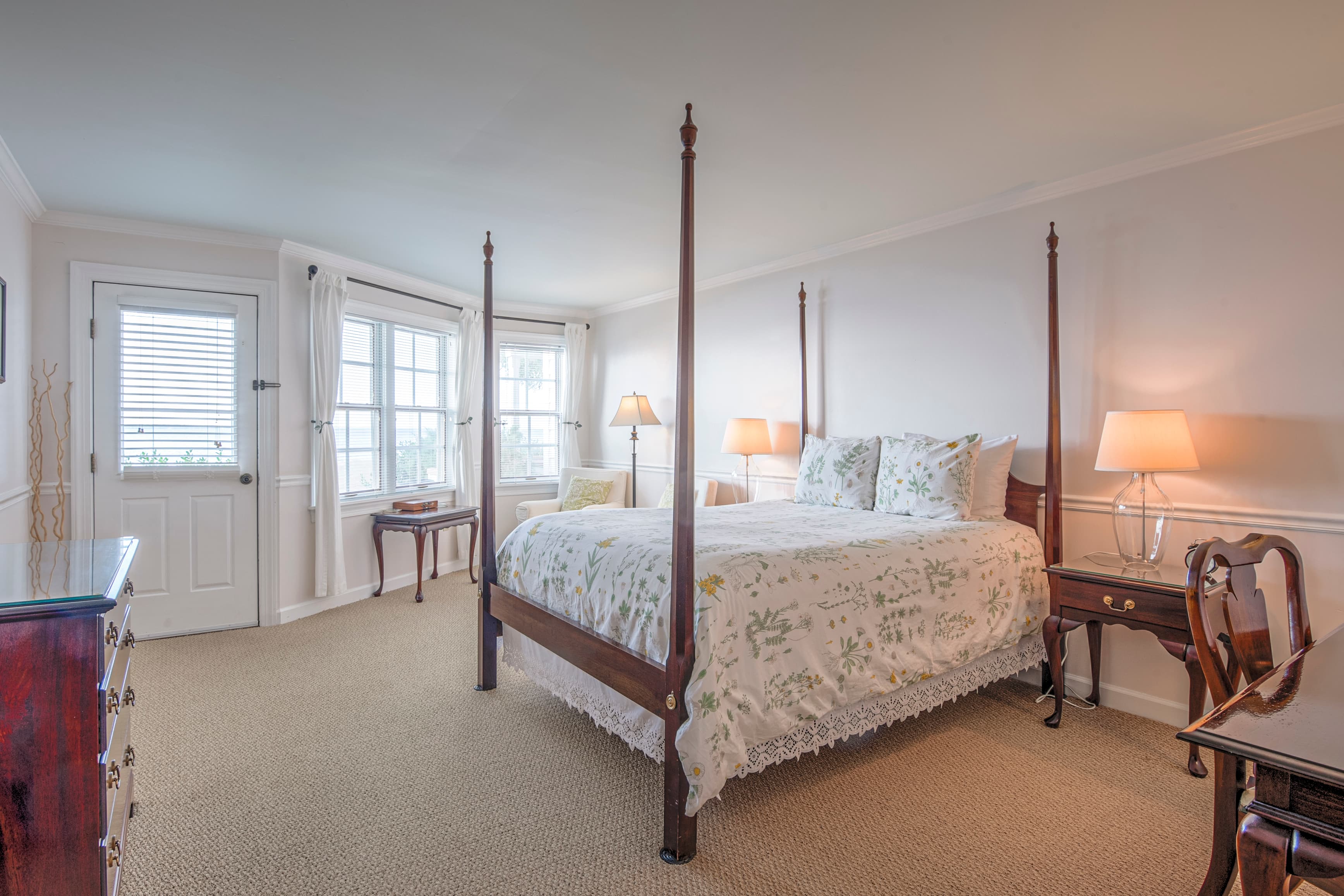 A cozy bedroom featuring a four-poster bed, two lamps, and large windows.
