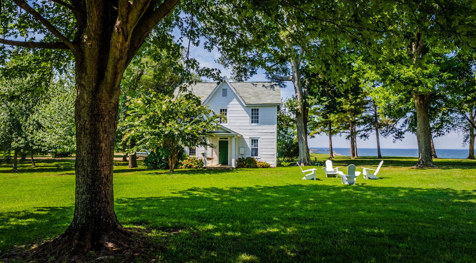 A quaint white house surrounded by lush greenery and a serene waterfront view.