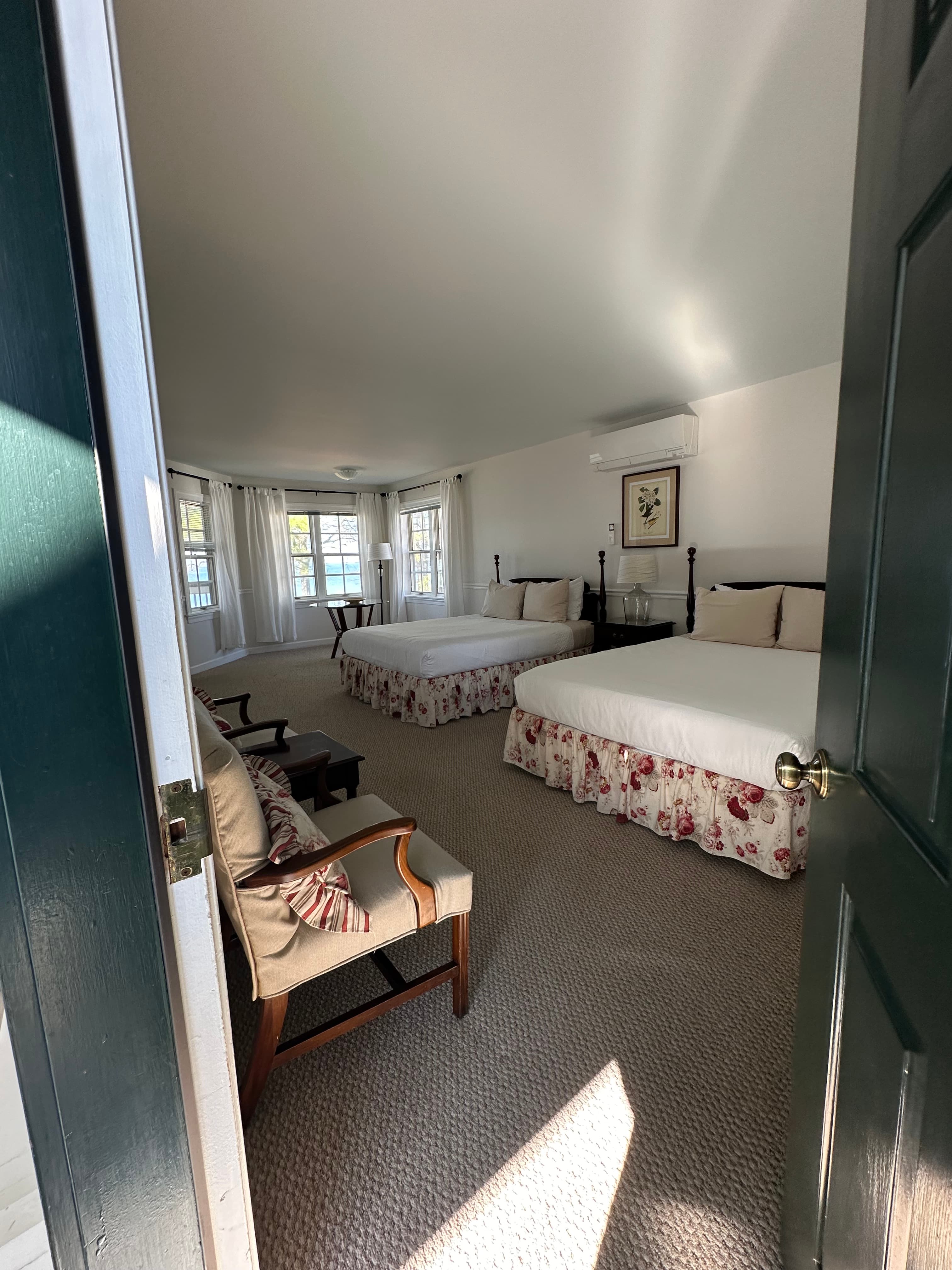 A spacious hotel room featuring two beds, a seating area, and large windows with natural light.