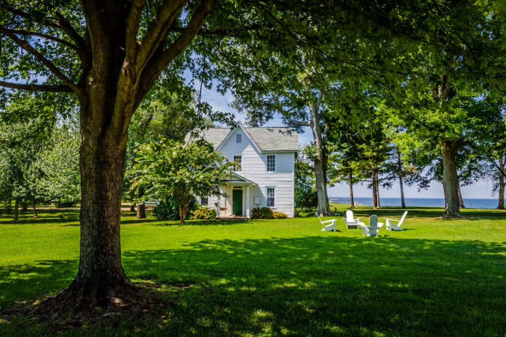 A white house surrounded by lush greenery and white chairs on a manicured lawn near the water.